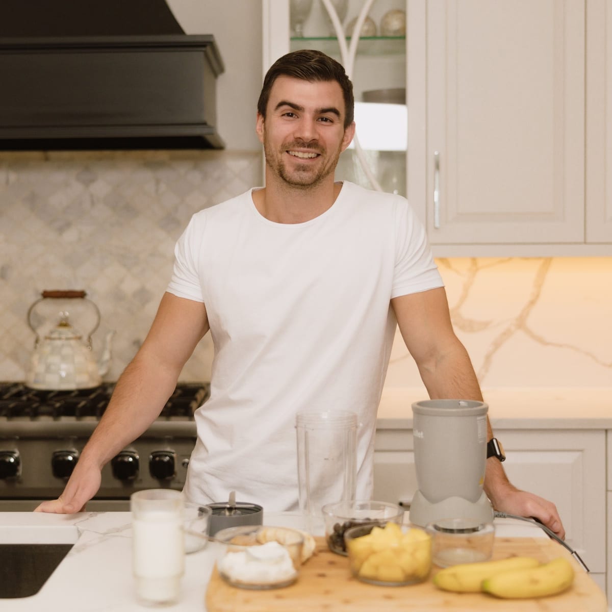 Nate Bladecki in a kitchen, with a blender, cut fruit, yogurt and milk on the counter.